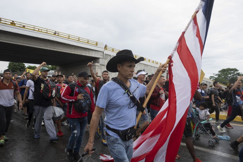 A migrant carries a U.S. flag as he pulls luggage during a migrant caravan leaving the city of Tapachula in Chiapas state, Mexico, early Monday, June 6, 2022. Several thousand migrants set out walking in the rain early Monday in southern Mexico, tired of waiting to normalize their status in a region with little work still far from their ultimate goal of reaching the United States. (AP Photo/Isabel Mateos)