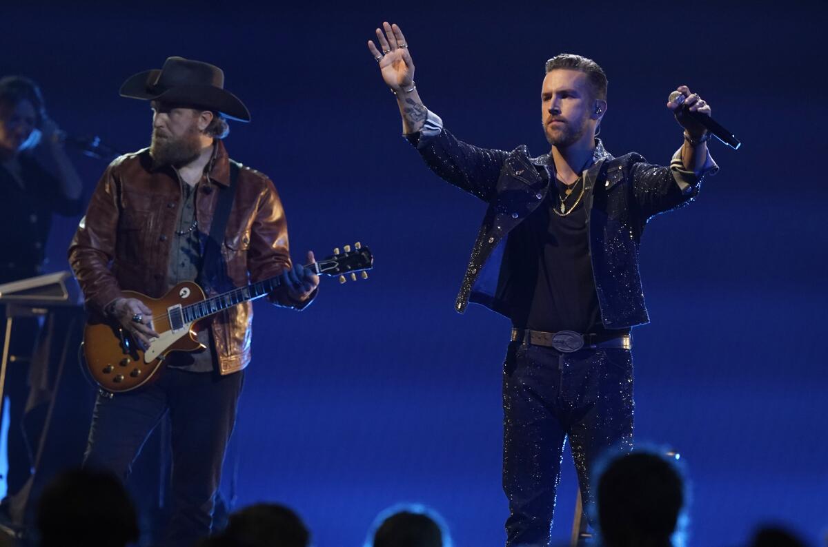 A man plating an electric guitar and another man waving with a microphone in one hand