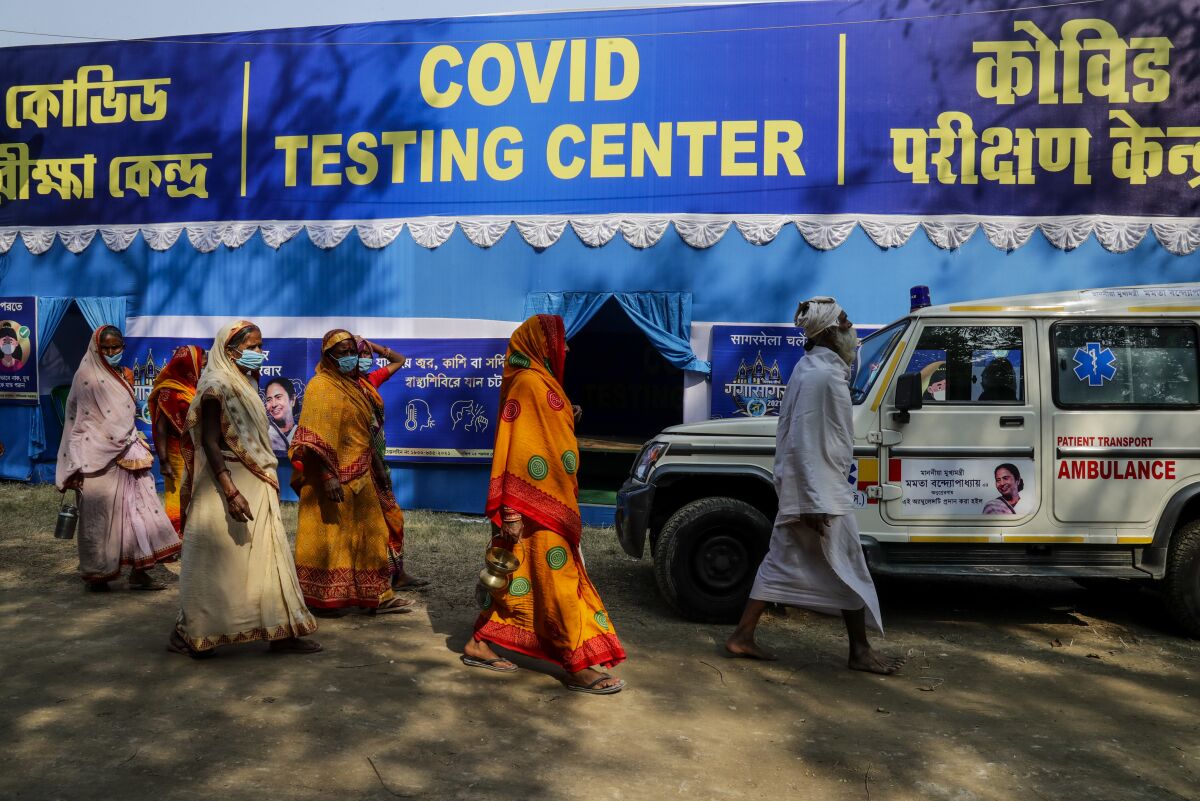 Hindu pilgrims walk past a tent with a banner that says "Covid testing center."