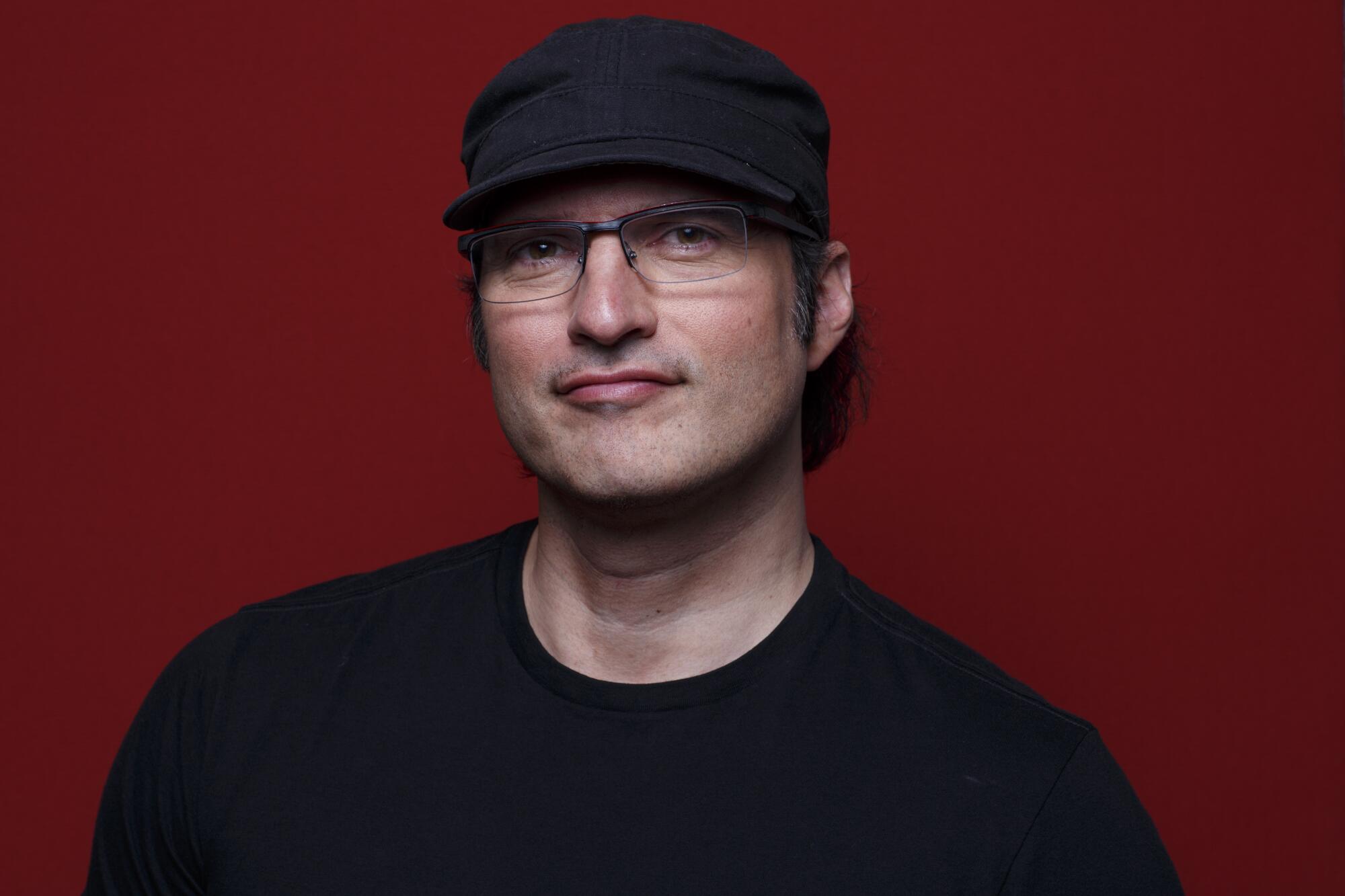 A man wearing glasses and a dark T-shirt and hat