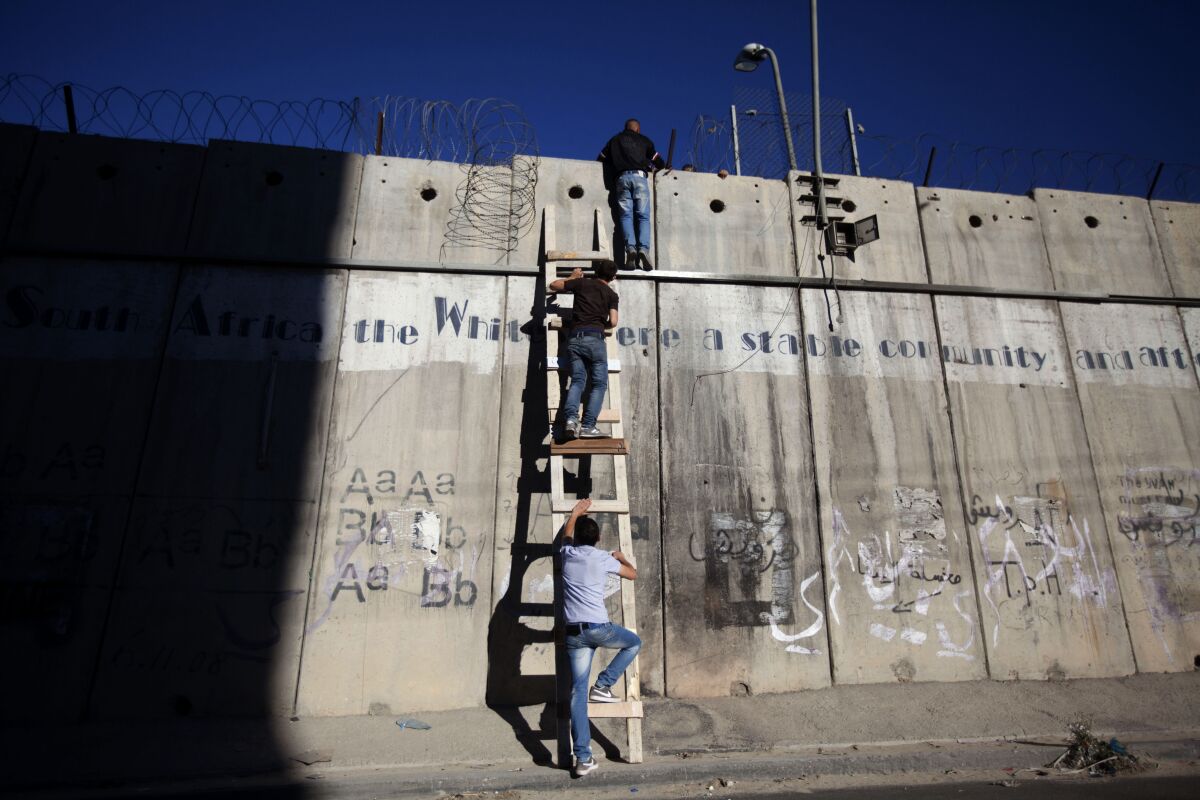 People climbing a ladder against Israel's security barrier