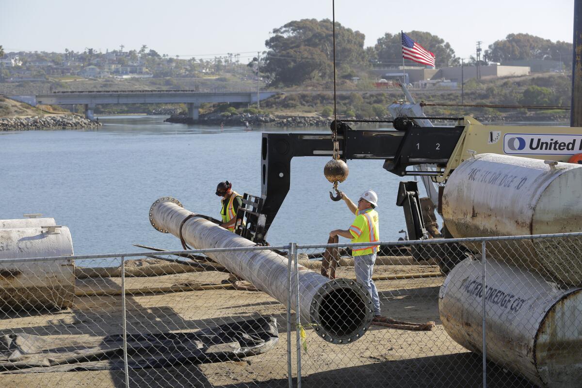 Workers move sections of pipe at the west edge of Agua Hedionda Lagoon in Carlsbad Friday. photo by Bill Wechter