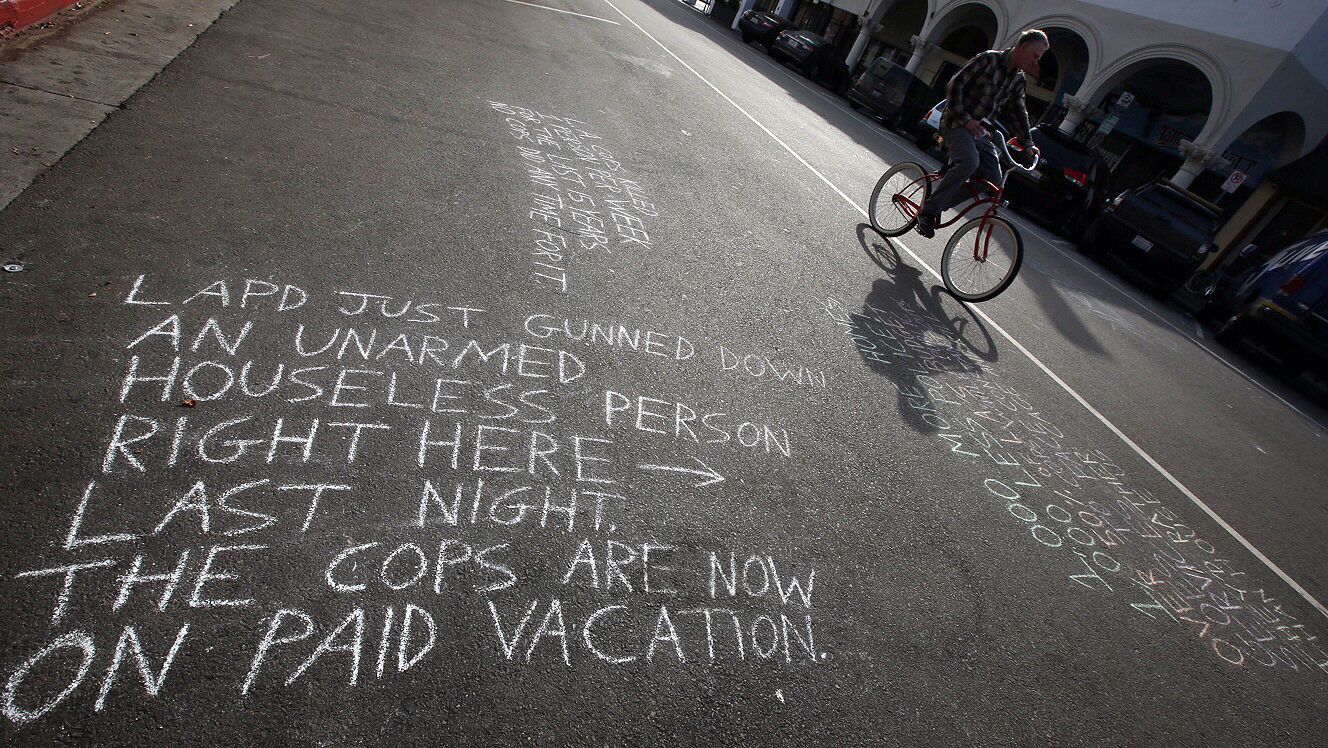 A man on a bike pedals past a messages written in chalk near the site of a fatal LAPD officer-involved shooting of a homeless man.