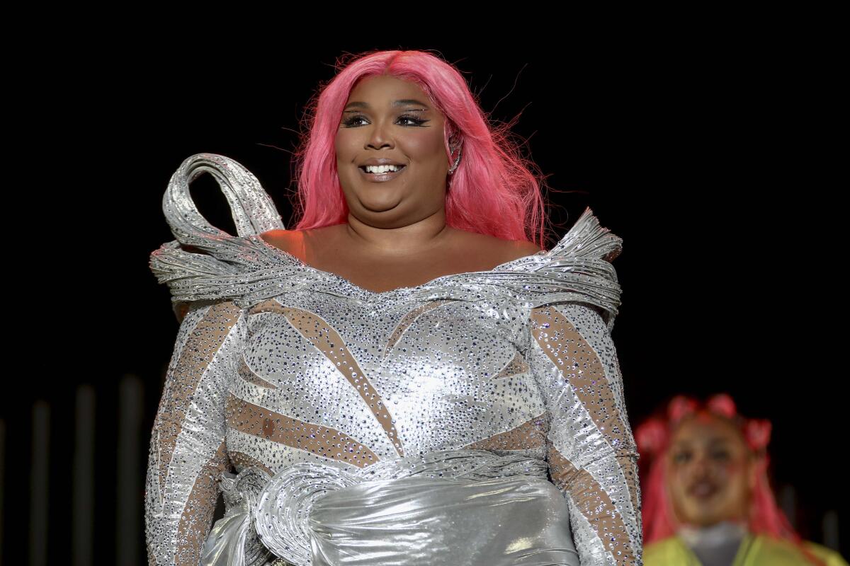 Lizzo smiling in a sparkly silver bodysuit and bubblegum pink wig.