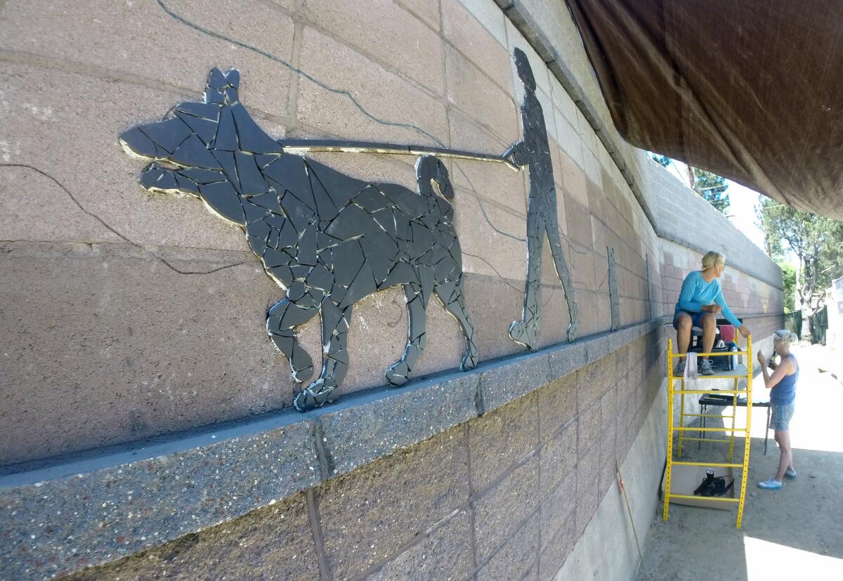Artist Miriam Balcazar, sitting, continues her work, with the help of her visiting sister Eugenia Escarra, on a porcelain tile mural on a sound-wall between Indiana Avenue and Union Street along the south side of Curran Street in La Cañada Flintridge on Tuesday, July 8, 2014.