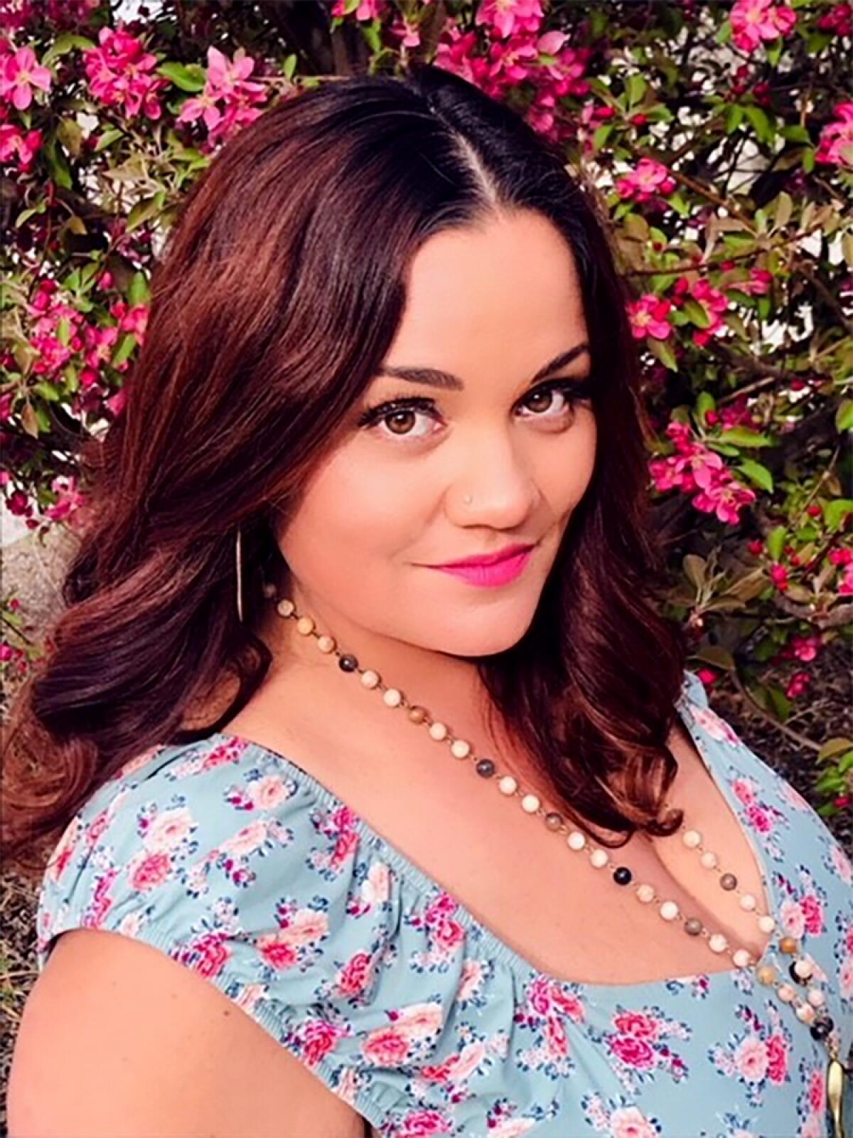 Jennifer Givhan, in a floral blouse, stands in front of flowers.