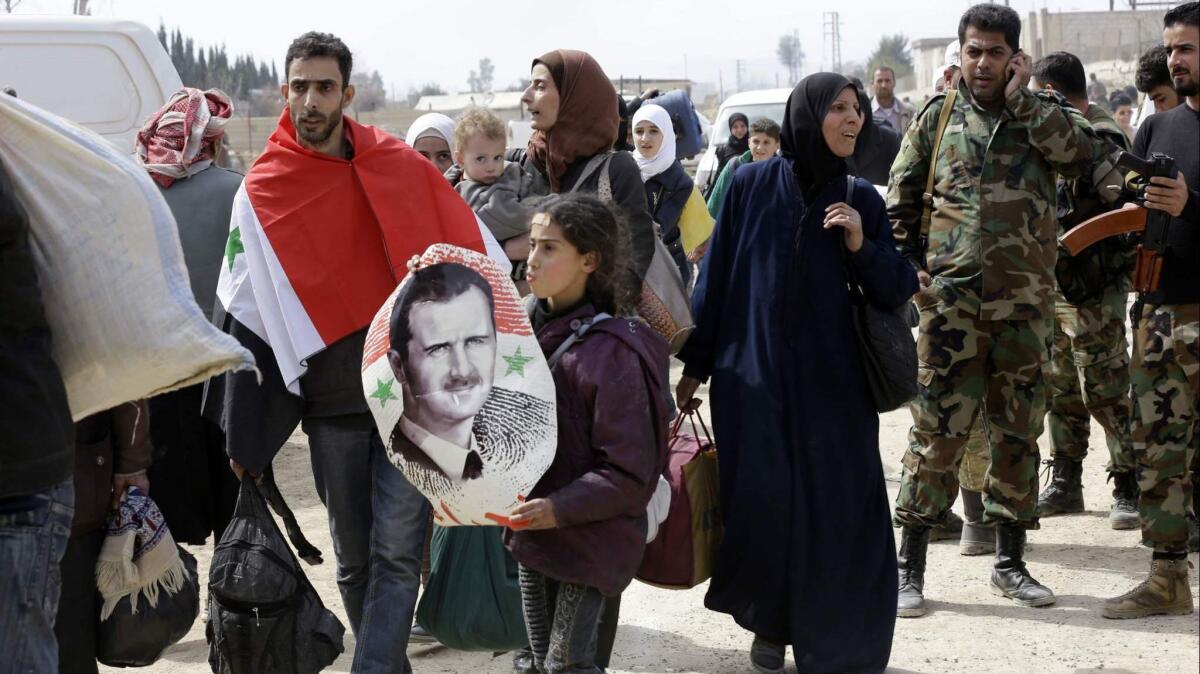 A Syrian man draped in the national flag walks with a girl carrying a poster of Syrian President Bashar Assad during an exodus from rebel-held eastern Ghouta.