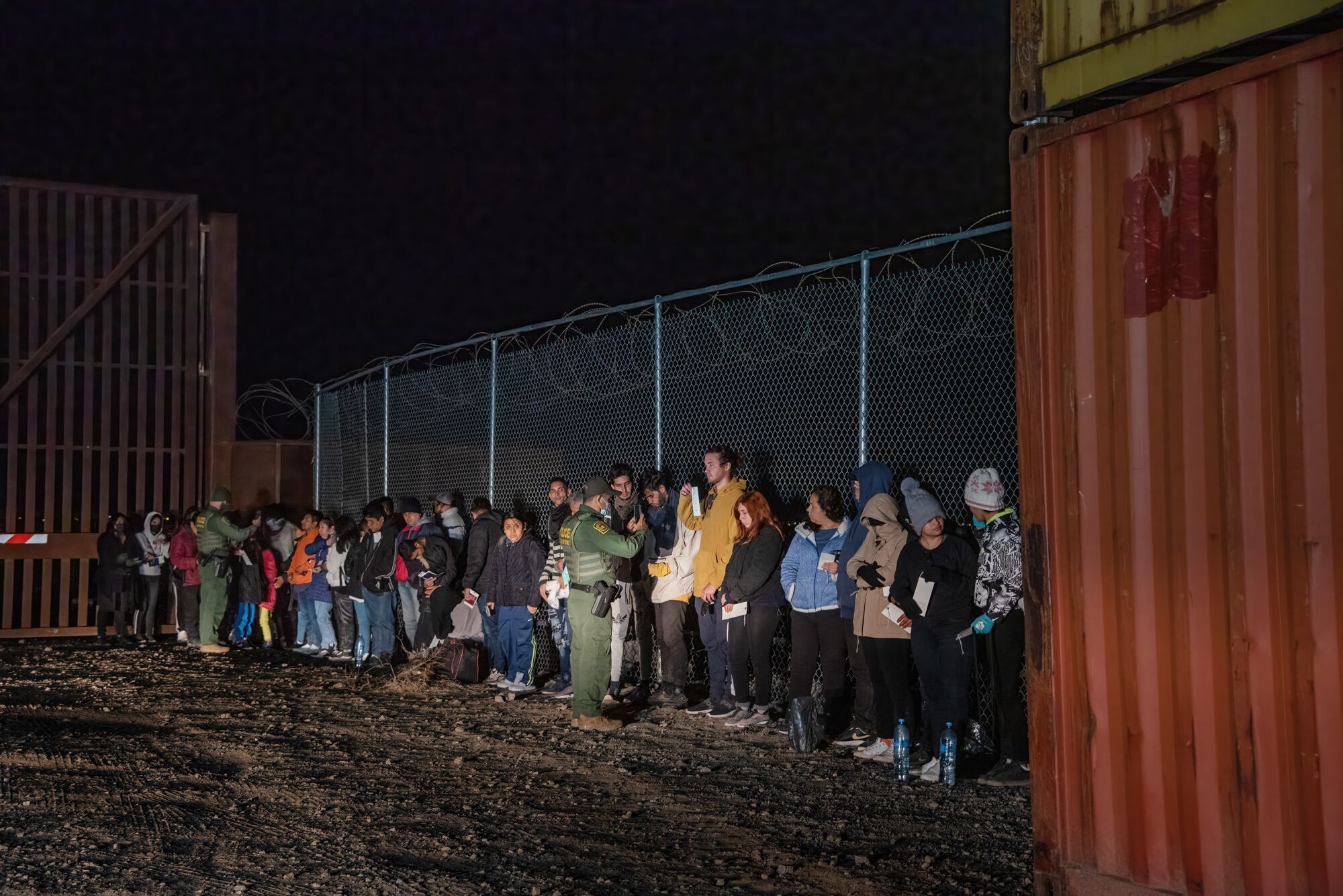 İki ABD Sınır Devriyesi ajanı, Meksika/Arizona sınırını geçtikten sonra teslim olan yaklaşık 100 kişinin bir bölümünü fotoğraflıyor.