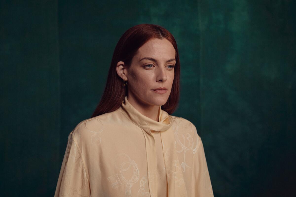 Riley Keough looks pensive in a long-sleeved blouse with a self-tie and long hair tucked behind her ears