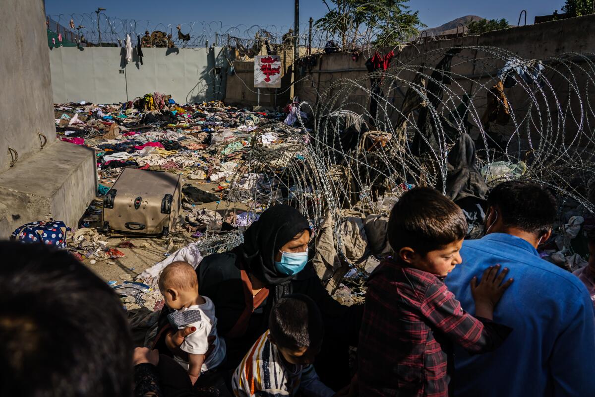 A family crouches in front of a barbed wire barrier