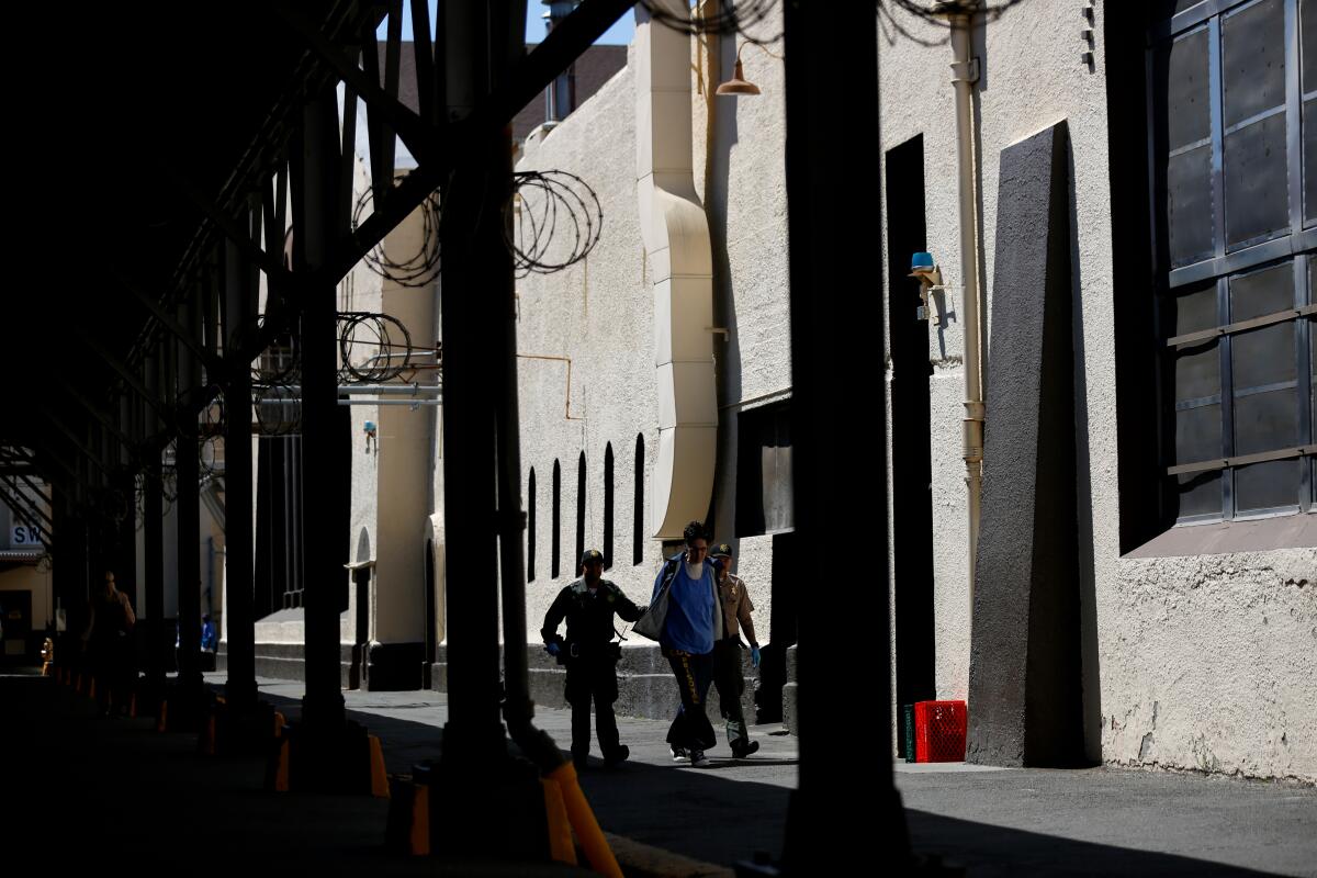 Two San Quentin guards walk a prisoner through a yard.