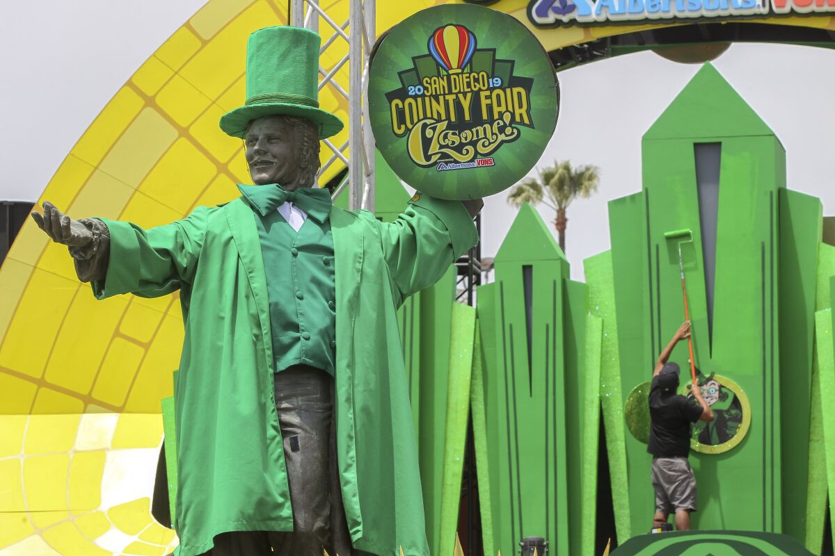 With the Don Diego statue dressed as the Wizard of Oz in the foreground, Andy Mazon paints a depiction of the Emerald City at the front entrance of the San Diego County Fair on Thursday in Del Mar. The fair opens Friday.