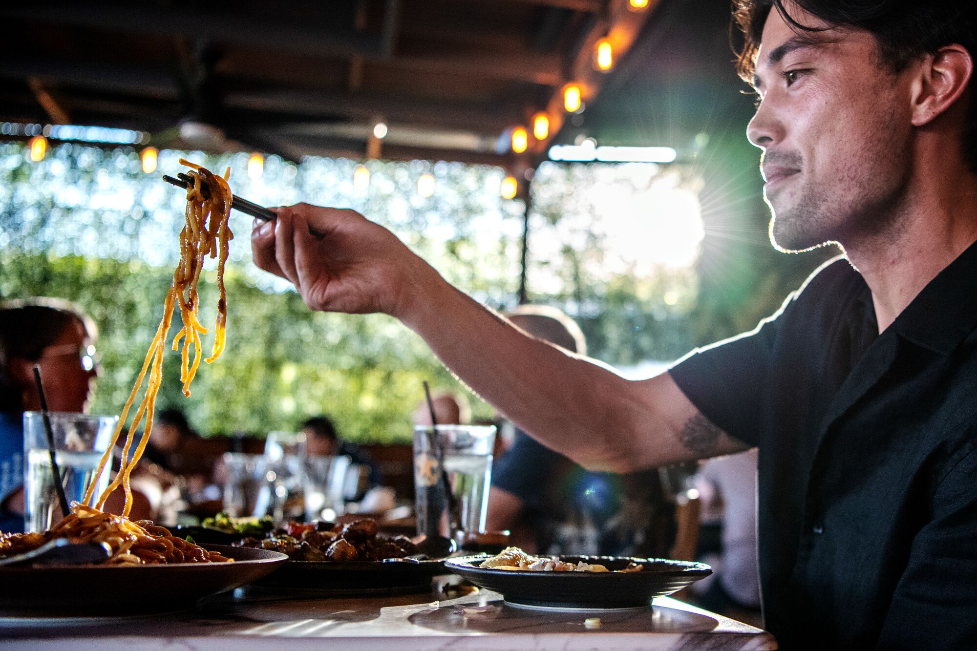 A man pulling noodles from a steaming bowl at a restaurant.