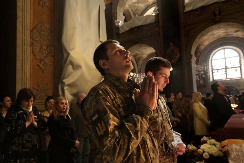 Lviv, Ukraine-April 30, 2022-At the Saints Peter and Paul Garrison Church in Lviv, Ukraine, soldiers attend Sunday mass along with civilians on May 1, 2022. (soldiers would not give names) Many of the icons, Christ and the angels, have been wrapped for protection from bombing, along with some of the stained glass windows. (Carolyn Cole / Los Angeles Times)