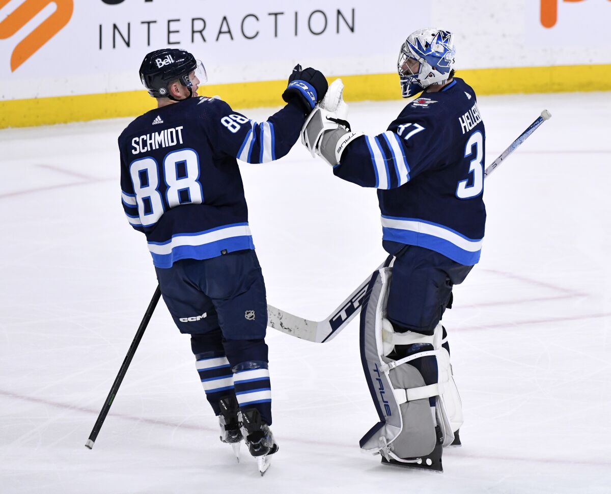 Winnipeg Jets goaltender Connor Hellebuyck (37) celebrates the win over the Arizona Coyotes with Nate Schmidt (88) during the third period of an NHL hockey game, Tuesday, March 21, 2023 in Winnipeg, Manitoba. (Fred Greenslade/The Canadian Press via AP)