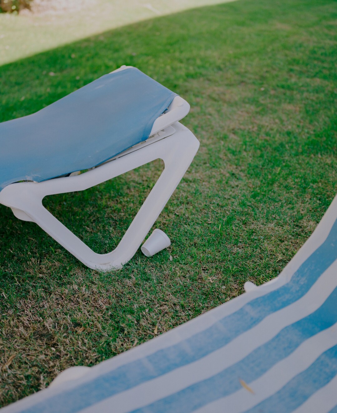 A portable seat on grass next to a blue and white striped towel.