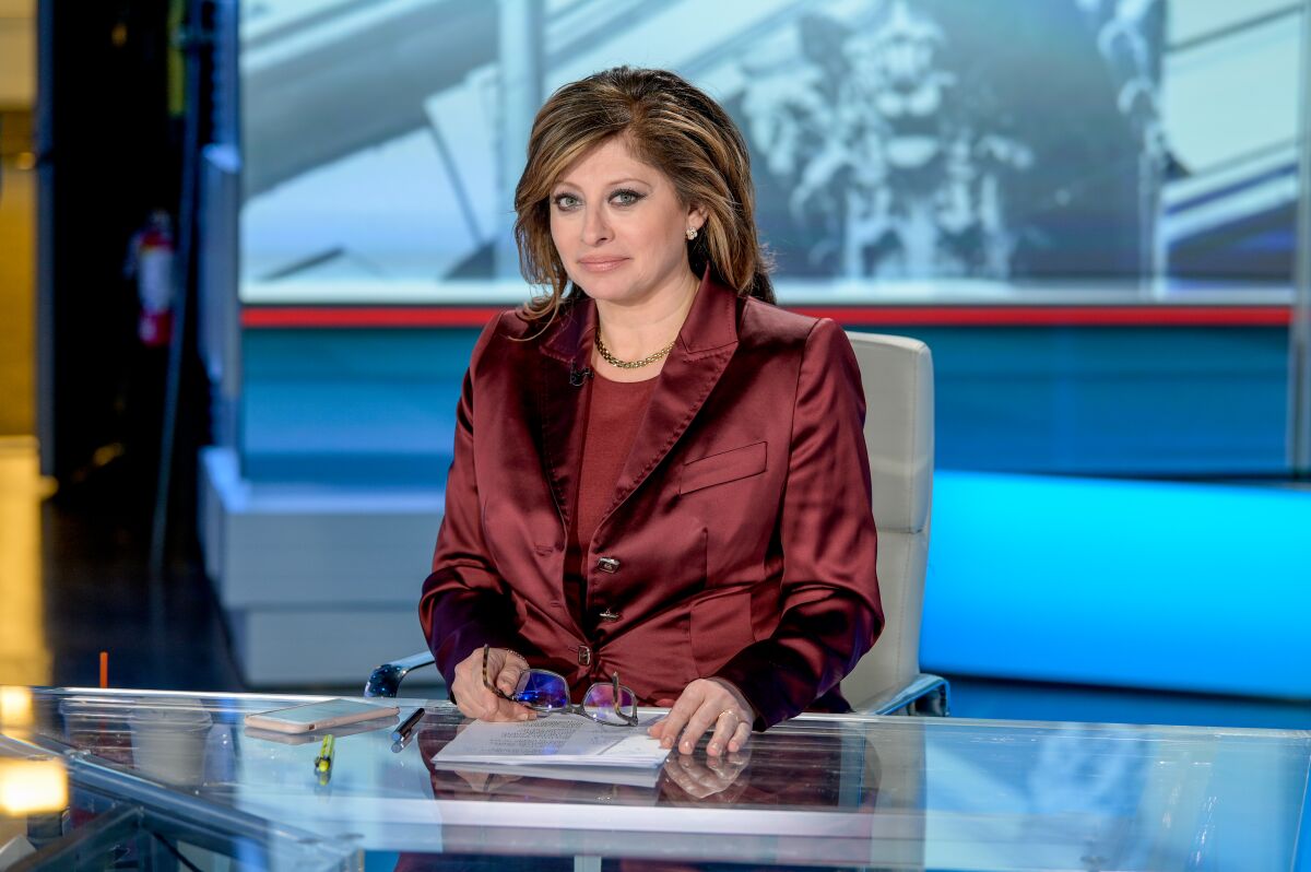 Maria Bartiromo looks at the camera while seated at a table with papers in front of her