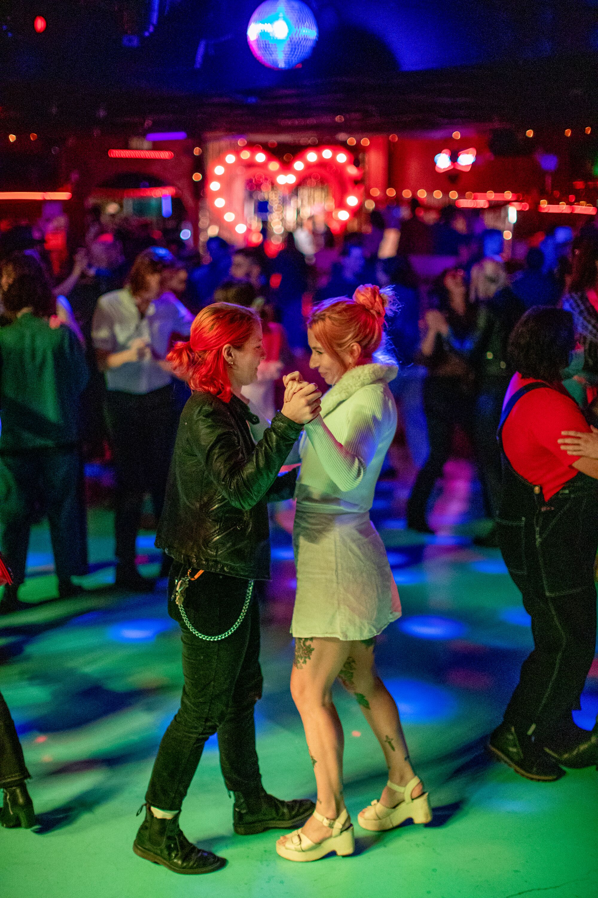 A couple of people dancing together on a dance floor, surrounded by others dancing under a disco ball. 