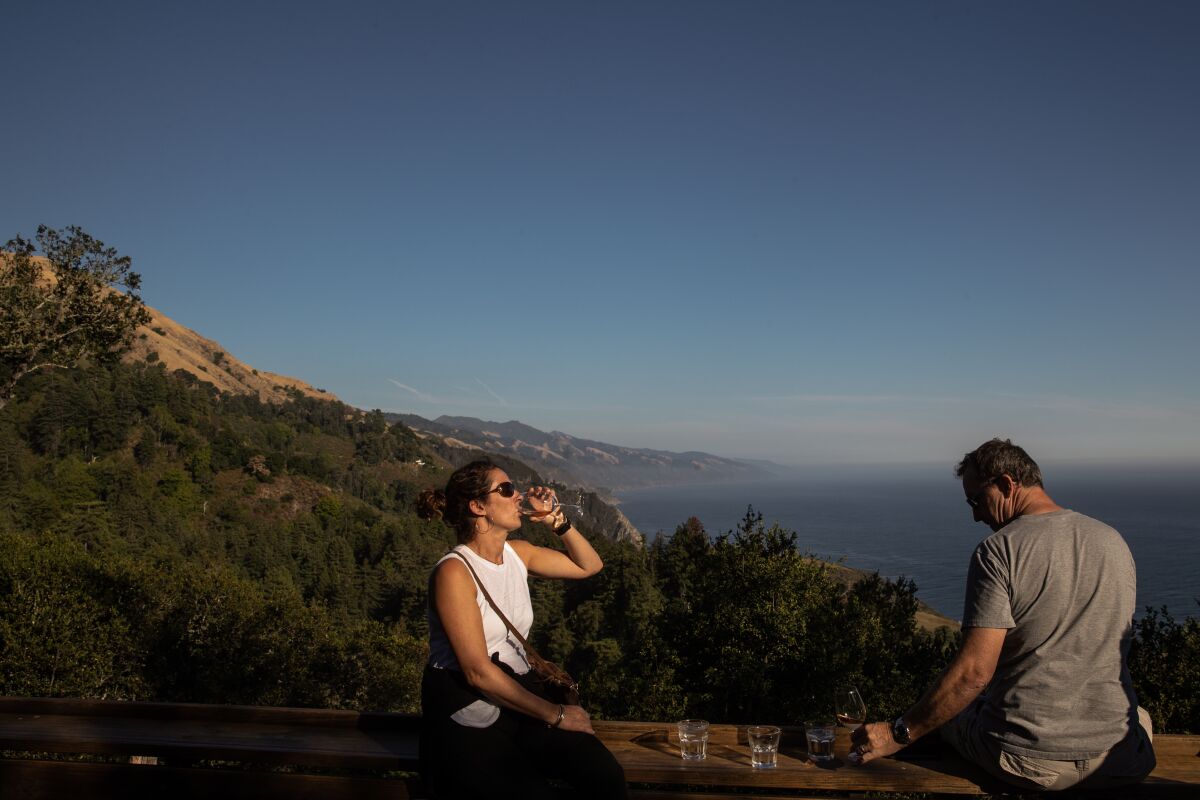 A couple enjoy cocktails on a deck perched on a Big Sur cliffside