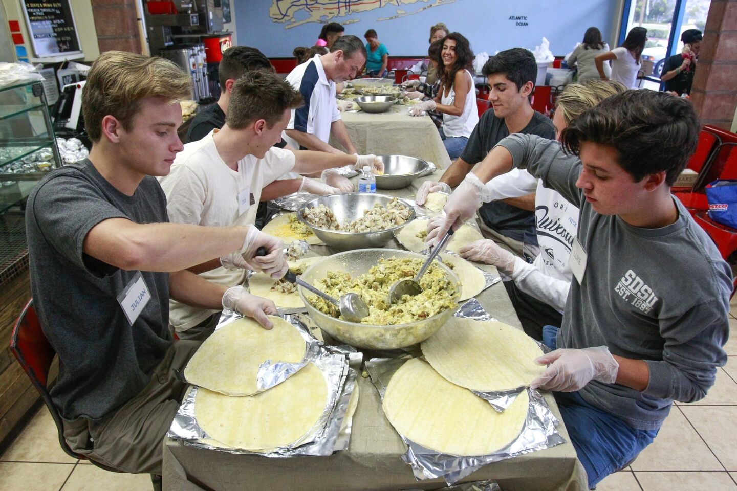 Burrito Boyz members Julian Wahl, left, and Luke Trolinger, both 18, spoon out scrambled eggs on to tortillas as they and other volunteers make egg burritos for homeless people at Long Island Mike's Pizza.
