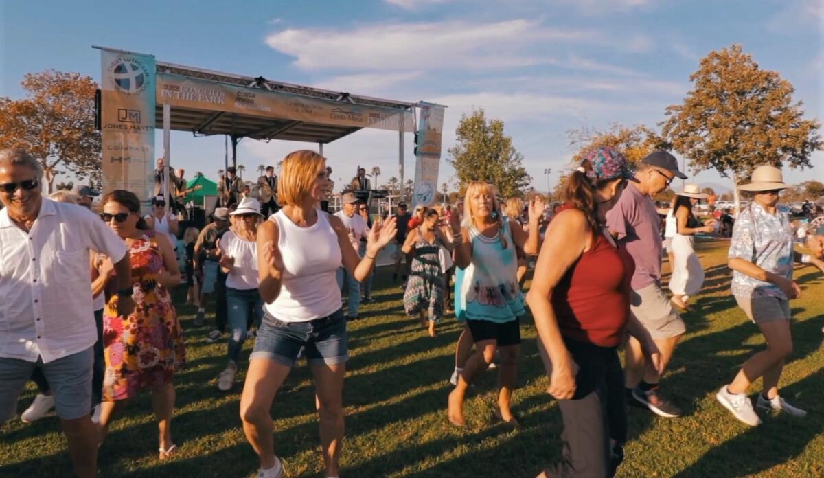 Residents dance under the setting sun in a line during Costa Mesa's Concerts in the Park summer series in 2022.