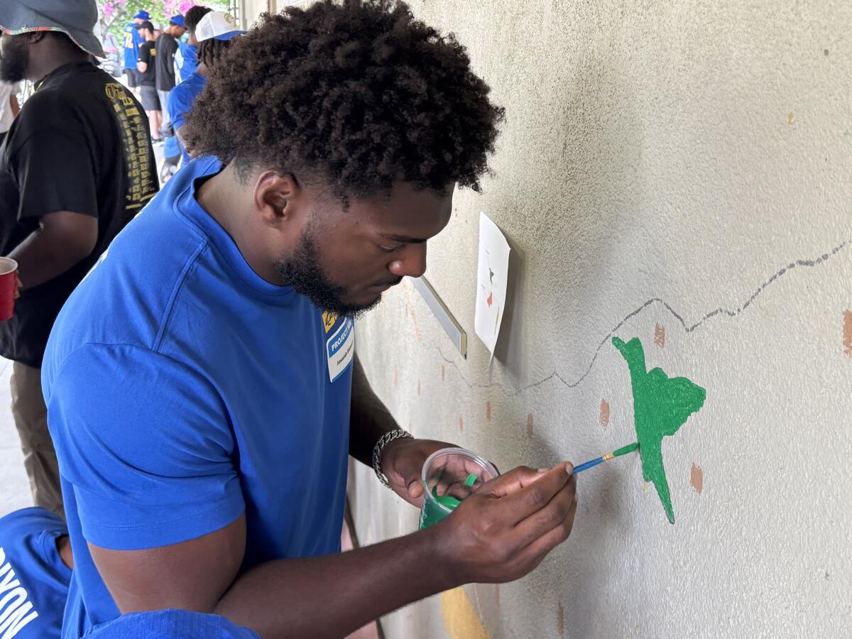 Rams rookie linebacker Josaiah Stewart paints a bird on a hallway wall at Odyssey Charter School in Altadena.