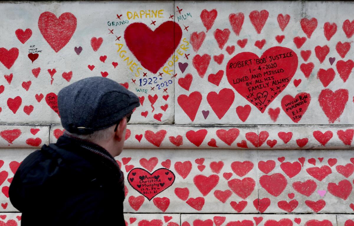 A man walks past the National Covid Memorial Wall commemorating all those who have died of coronavirus, on the Thames Embankment opposite the Houses of Parliament in London, Thursday, April 8, 2021. Bereaved families want the wall of painted hearts to remain a site of national commemoration and are asking the Prime Minister to help make the memorial permanent. (AP Photo/Frank Augstein)