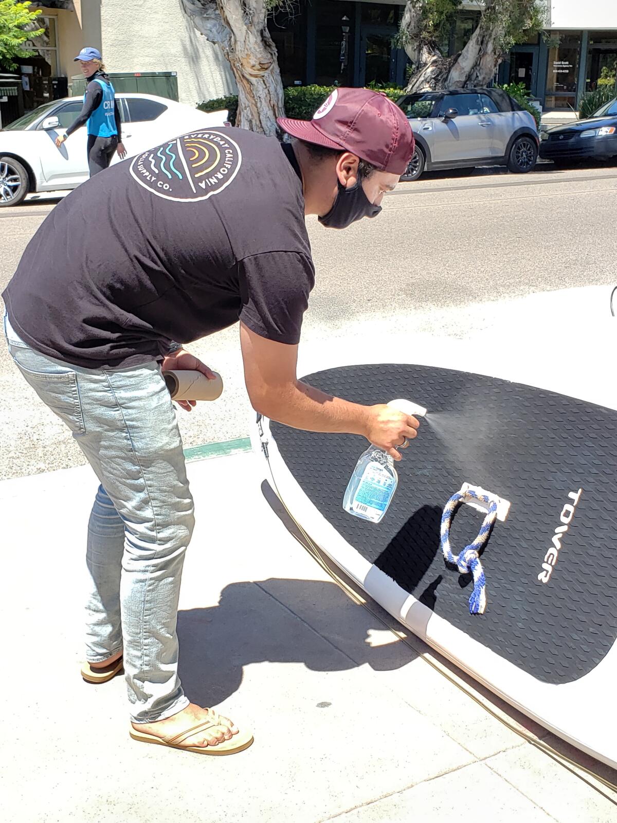 Everyday California General Manager Kama Hurwitz cleans a paddleboard with sanitizing spray.