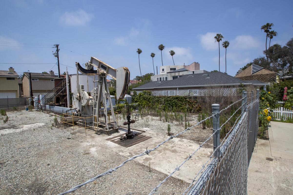 An oil pump jack in a lot surrounded by barbed wire next to homes