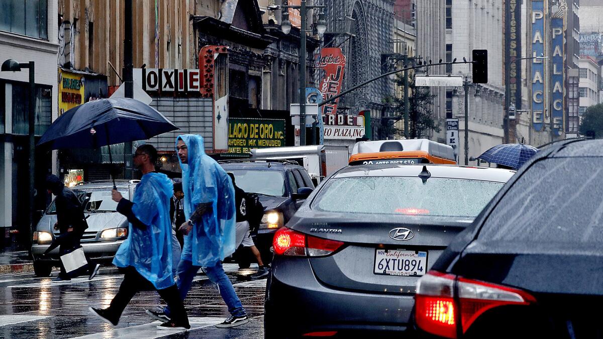 Pedestrians walk in the rain at the intersection of Broadway and Fifth Street in downtown Los Angeles on Saturday, Mar. 2, 2019.