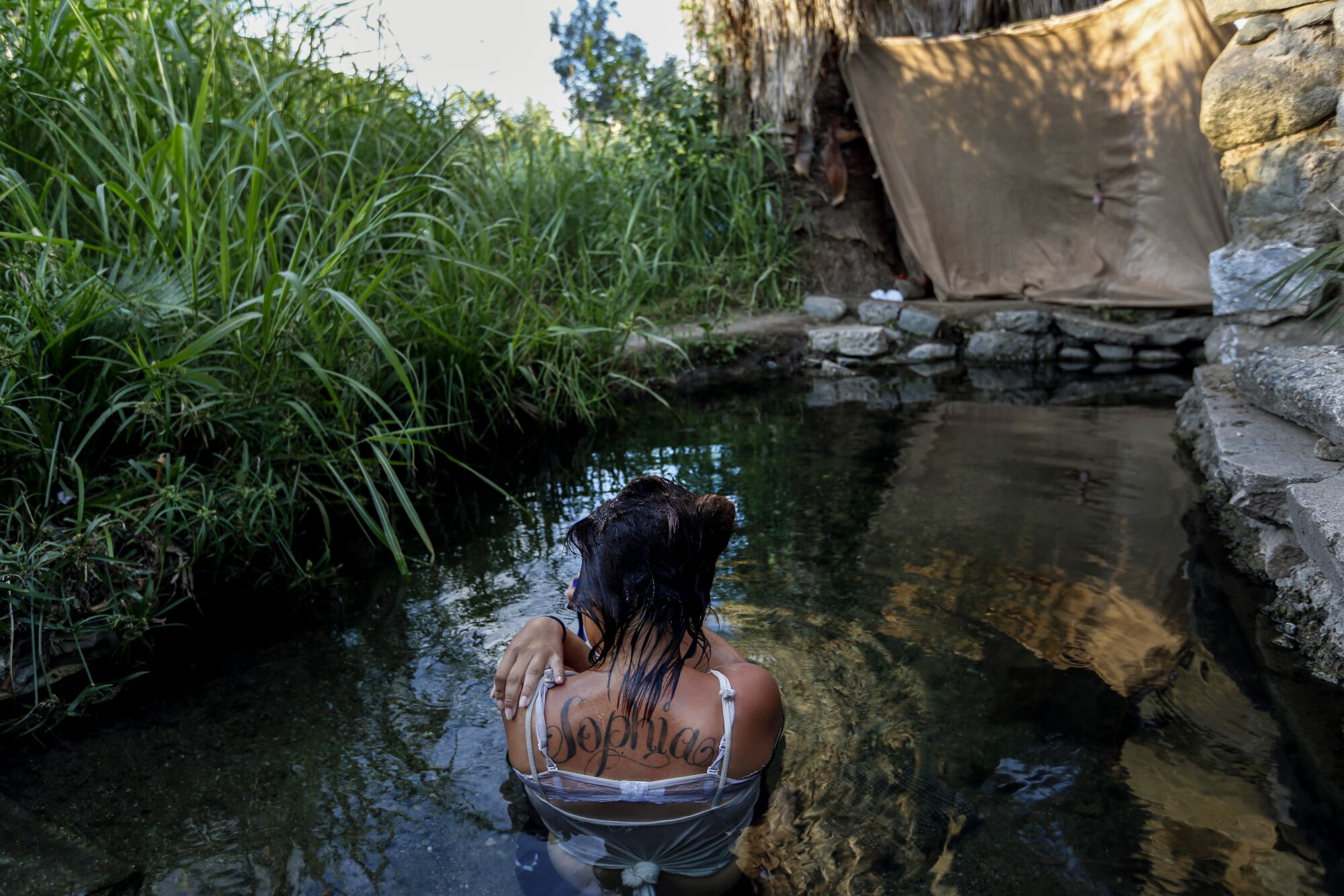 A woman soaking in a pond is seen from behind