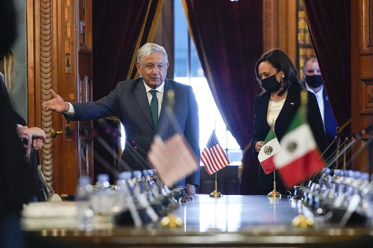 Kamala Harris and Andrés Manuel López Obrador stand at a table lined with mini water bottles and small U.S. and Mexican flags