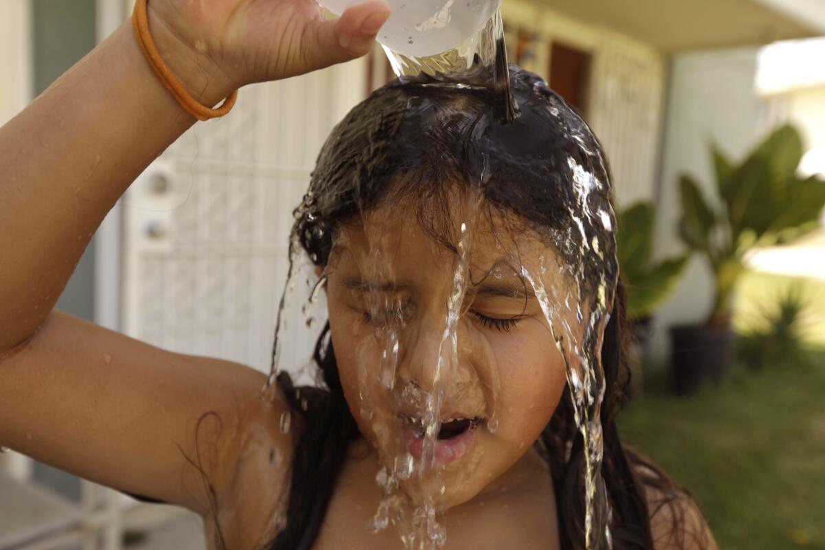 A girl pours a cup of water over her head to cool off on a hot afternoon in the San Fernando Valley.