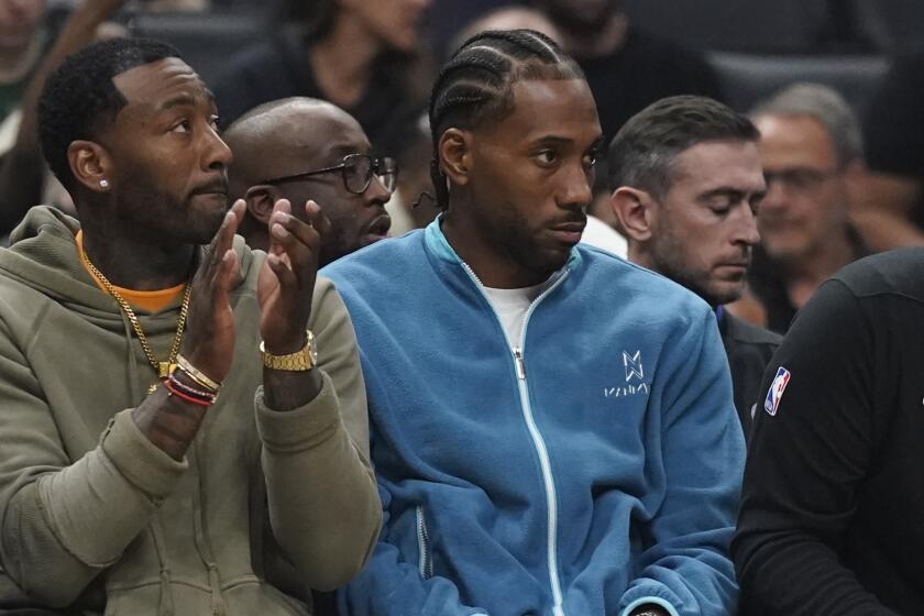 LA Clippers guard John Wall, center, and forward Kawhi Leonard, right, sit on the bench.