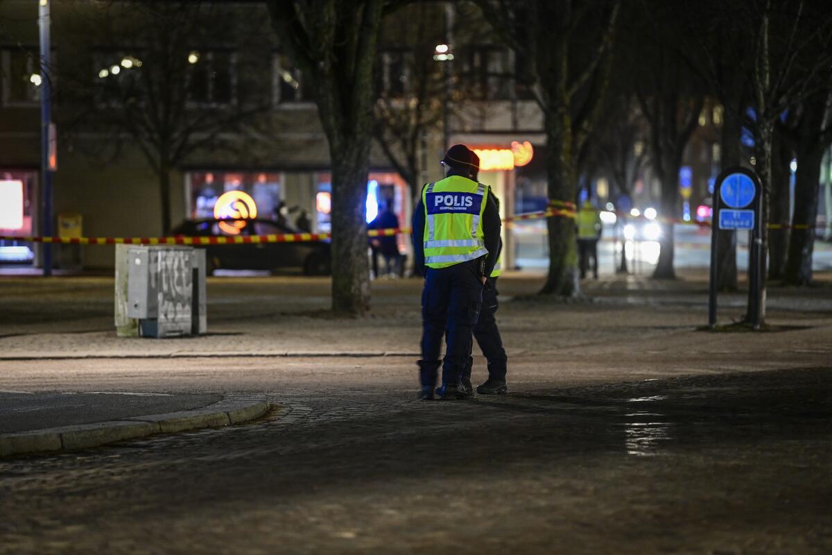 Police are seen in the area with shops, trees and walkways