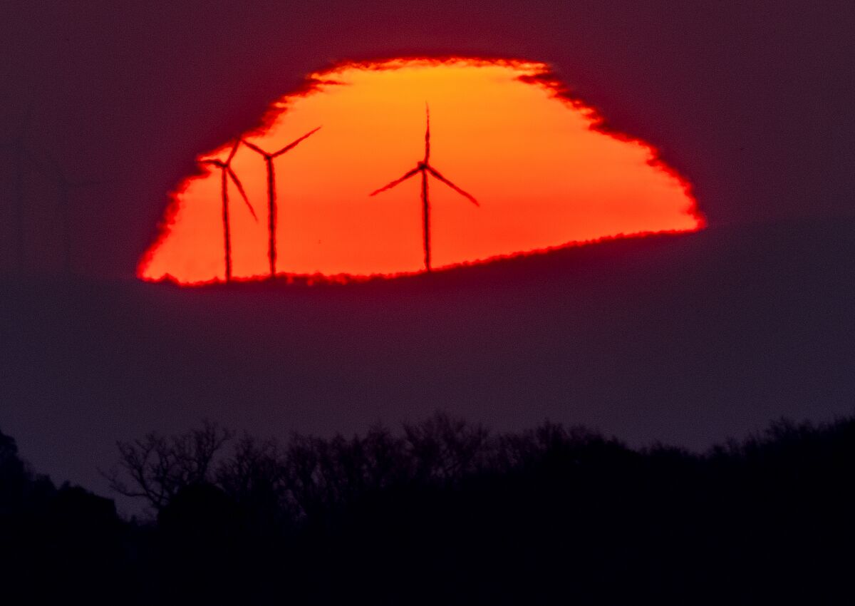 Wind turbines stand in front of the rising sun.