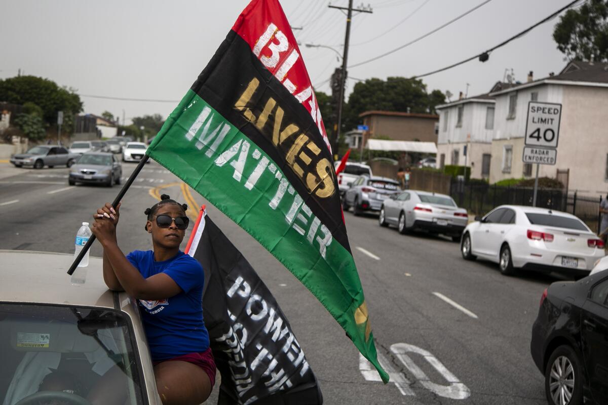 Deja Roquemore waves a flag as she is parked on Normandie Ave. during a protest in honor of Dijon Kizzee