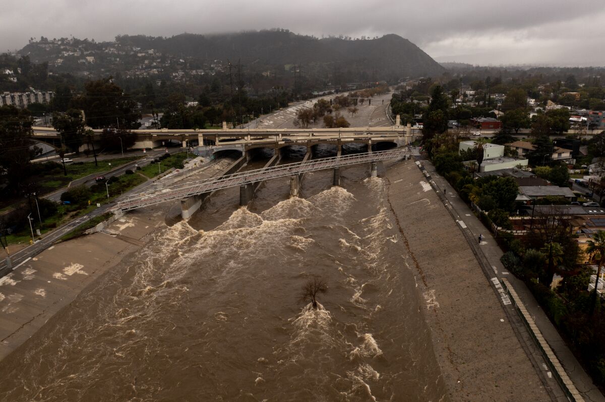 Brown water flows along the concrete embankments of the Los Angeles River.