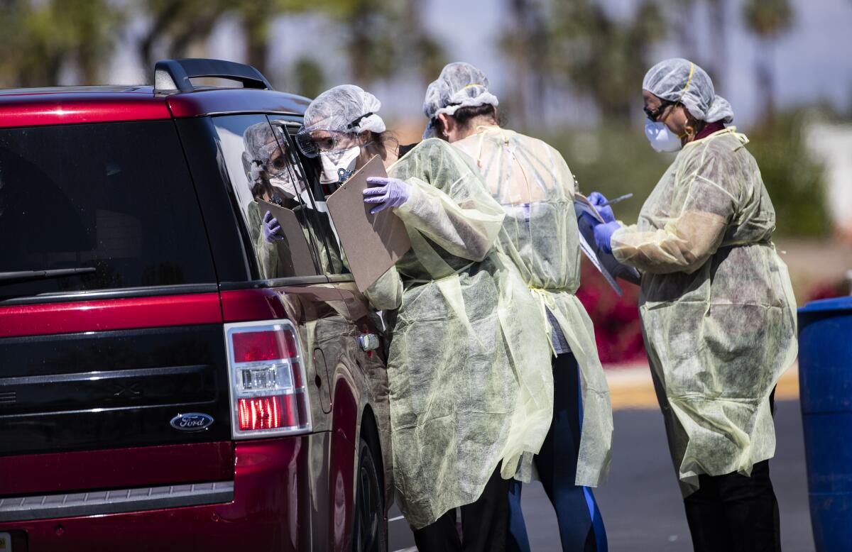 Riverside County medical personnel screen a car of four people at a coronavirus drive-though testing facility in Indian Wells.