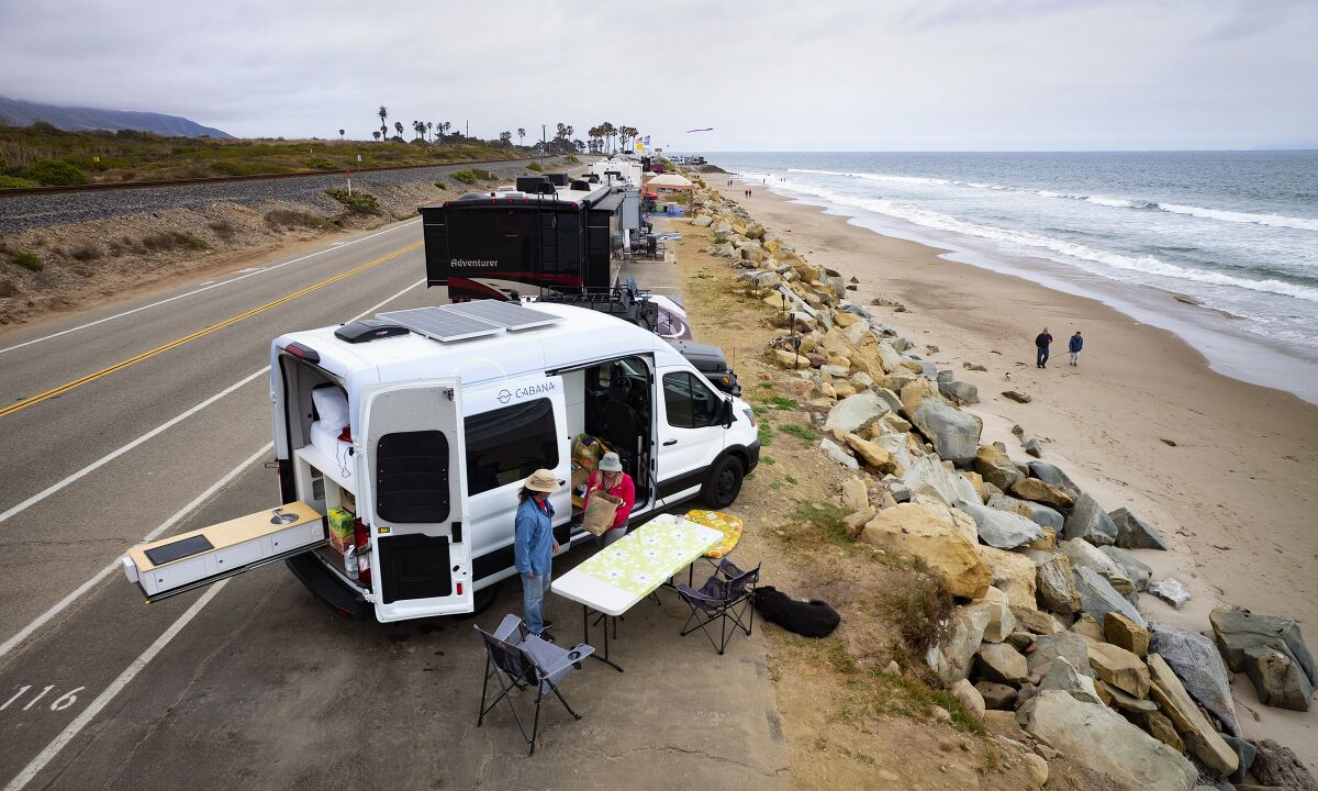 A couple set up a table and chairs next to a van along the beach