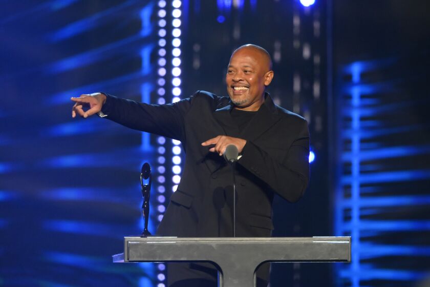 Dr. Dre wearing a black suit and pointing