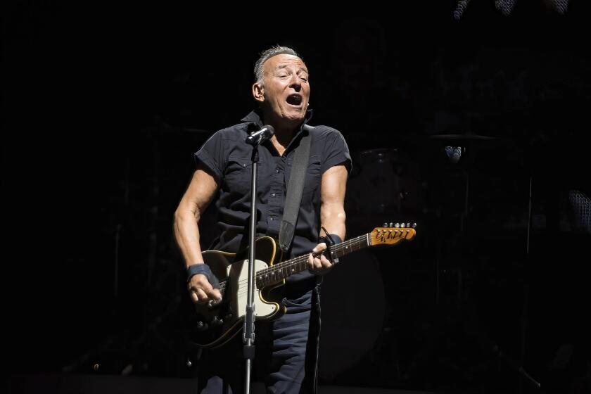 Bruce Springsteen sings on a dark stage while playing guitar