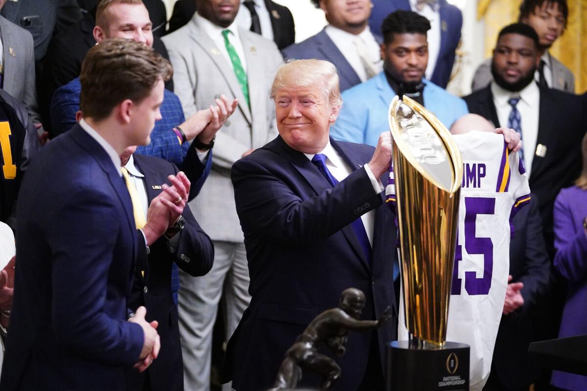 A smiling President Trump holds up a "Trump 45" LSU football jersey during the team's visit to the White House.