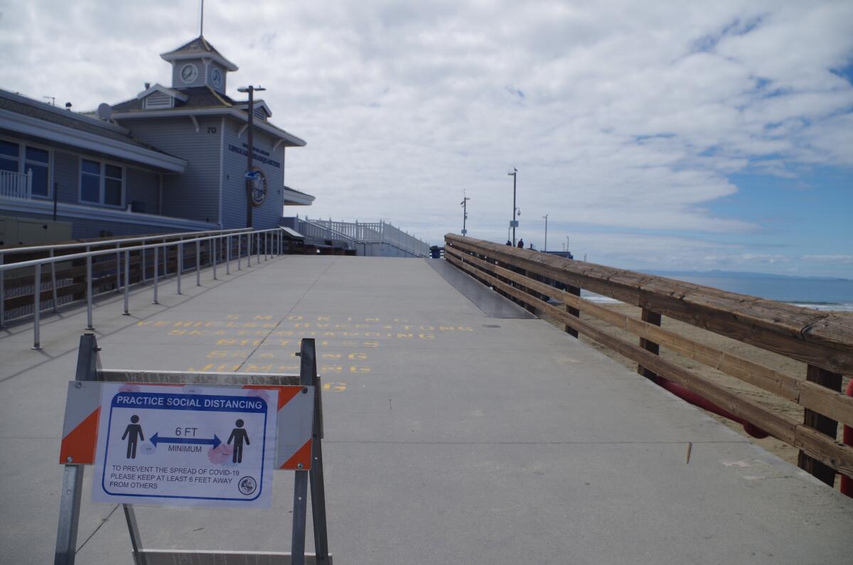 Signs remind visitors to Newport Pier to keep their distance to prevent spread of the coronavirus.