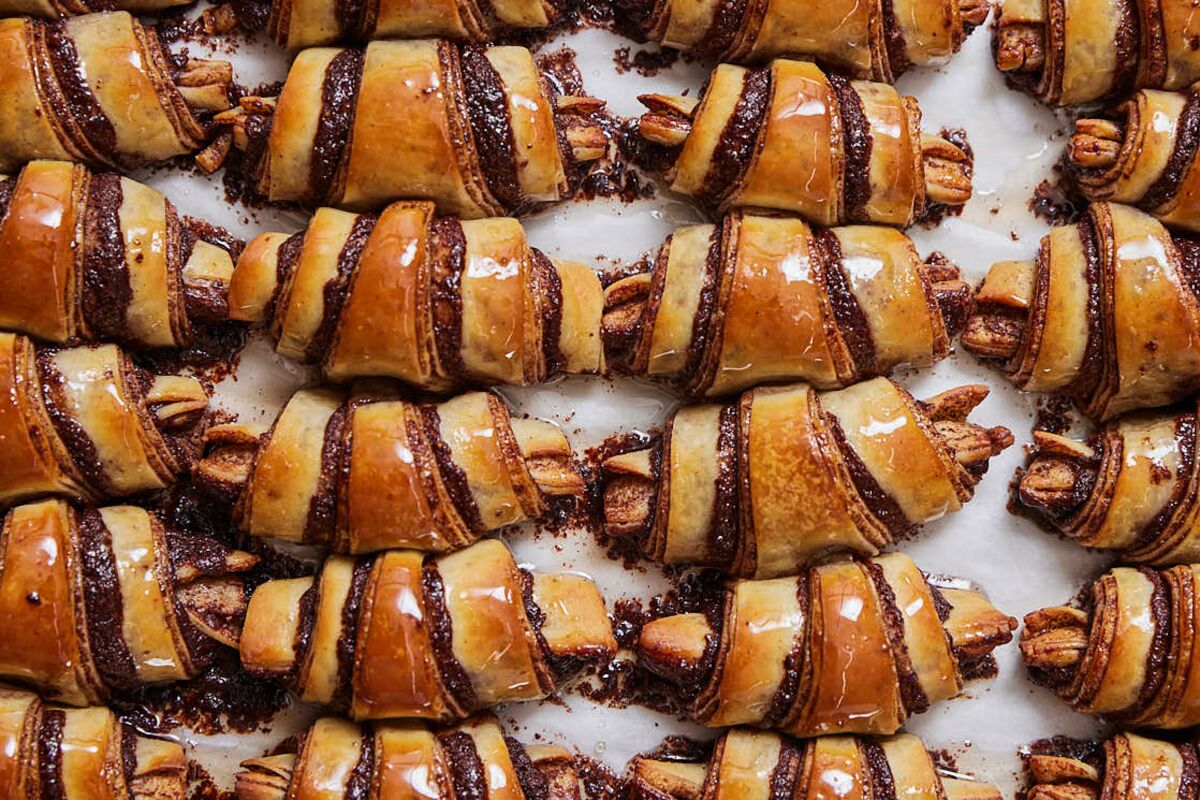 An overhead photo of a tray of horn-shaped, glossy chocolate rugelach.
