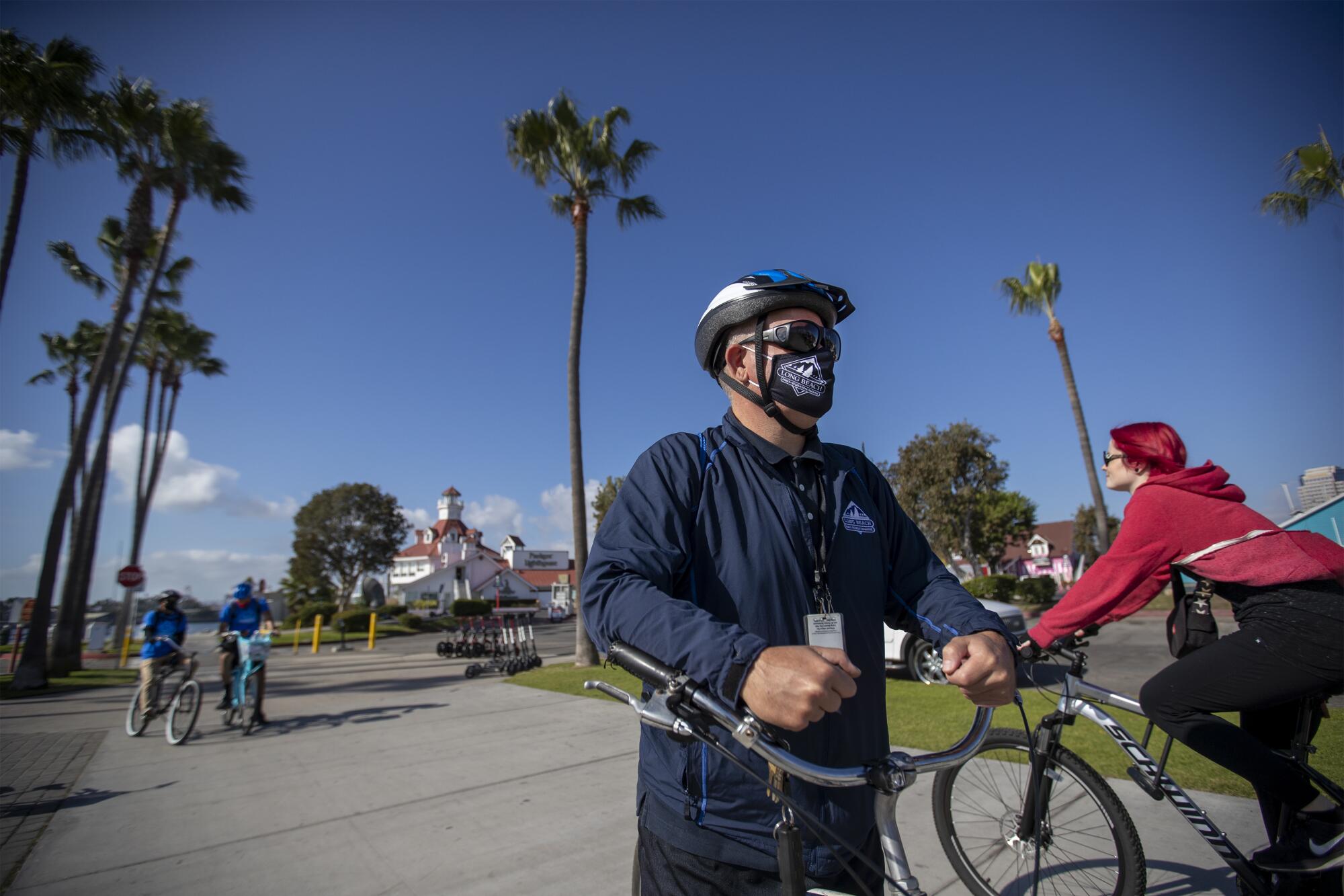 Bikers not wearing masks pass by Long Beach's health ambassadors Chris Bonomo, center, near Shoreline Village in Long Beach
