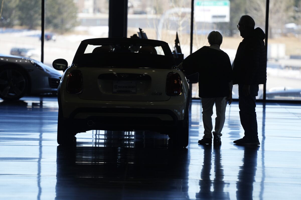 Car shoppers next to a 2022 Mini Cooper in an auto dealer's showroom