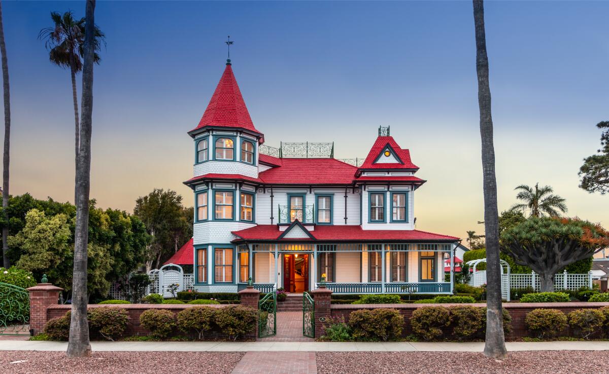 A photo of a large Victorian home with gardens and two palm trees