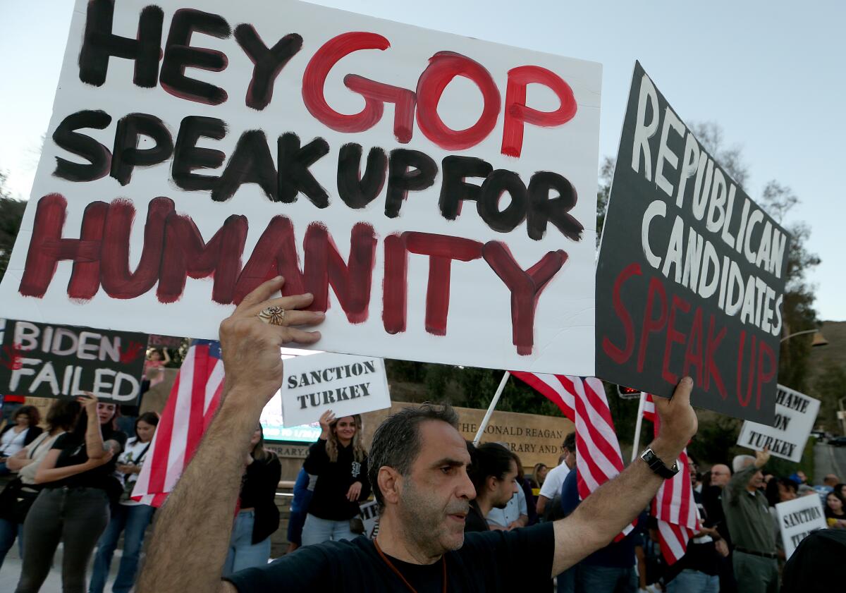 People hold signs in a crowd. One says "Hey GOP speak up for humanity."