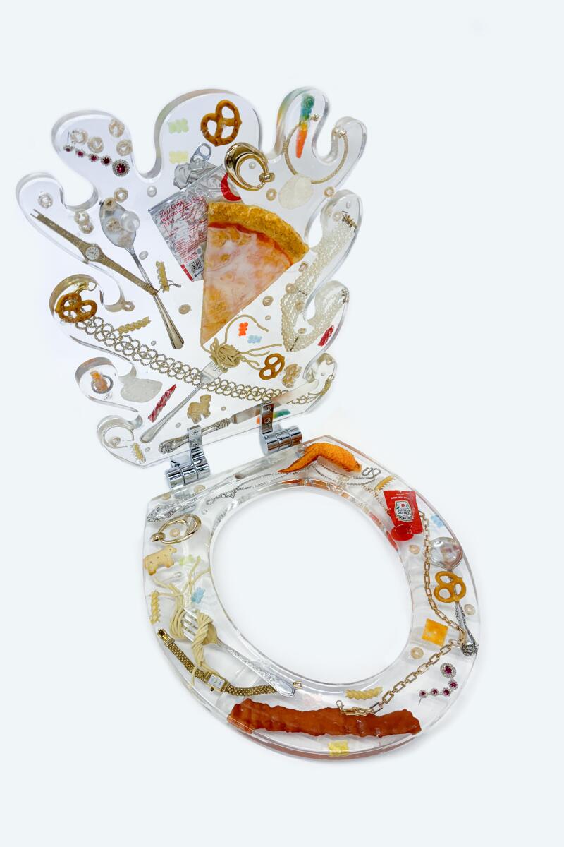 Bailey Hikawa, "Food and Jewelry" (2024), toilet seat featuring silver-plated fork, knife and spoon; fake diamond engagement ring; real pretzels; fake diamond earrings and necklaces; fake ketchup packet; fake chicken wing; real animal crackers; real Cheerios; fake milk; fake spaghetti; real Cheetos; fake pizza slice; Diet Coke can; fake gummy bears; real gummy worms; fake bacon; fake gold watch; real Cheez-It; fake pearl necklace.
